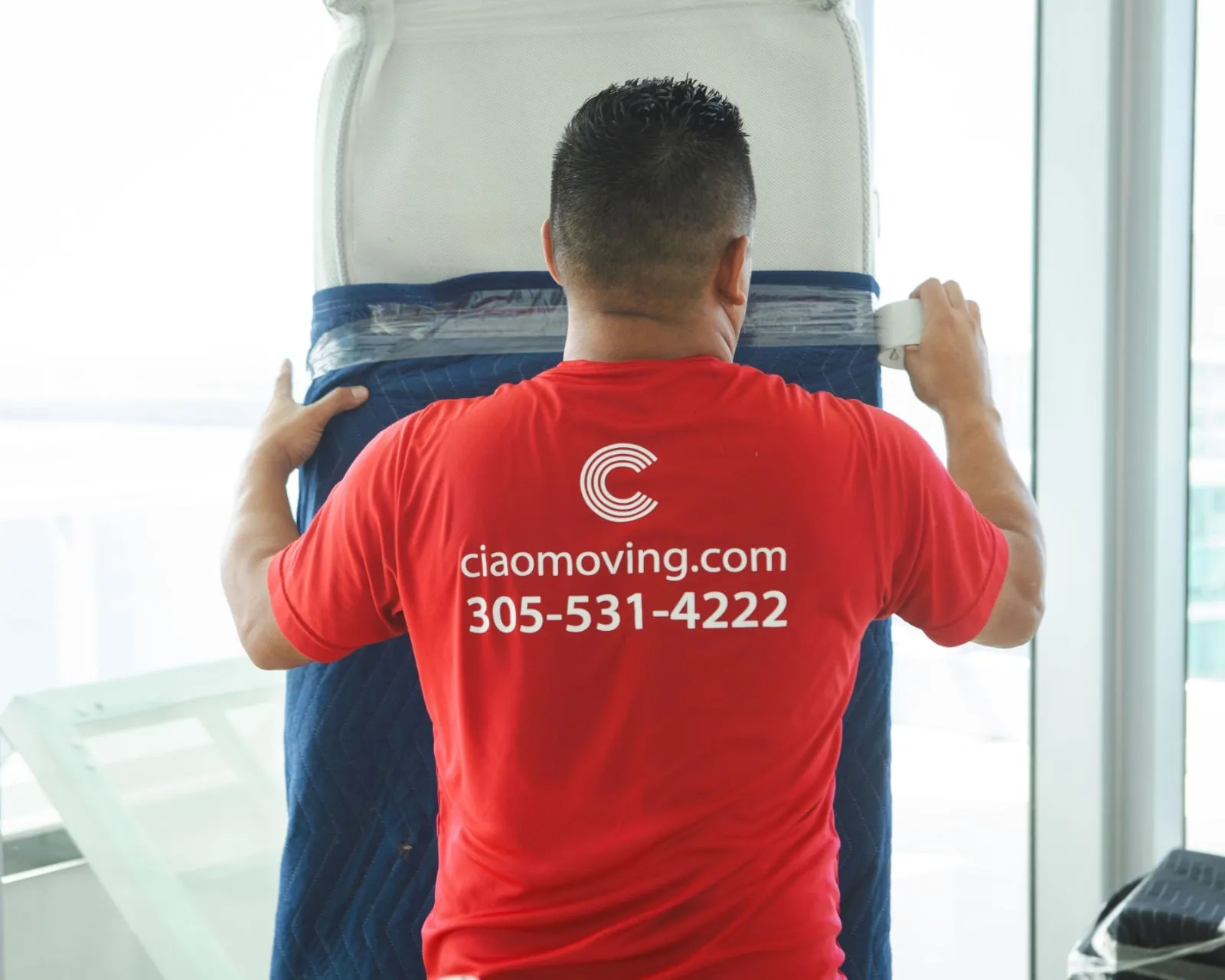 Ciao mover seen from behind in a red shirt printed with ciaomoving.com and the phone number
