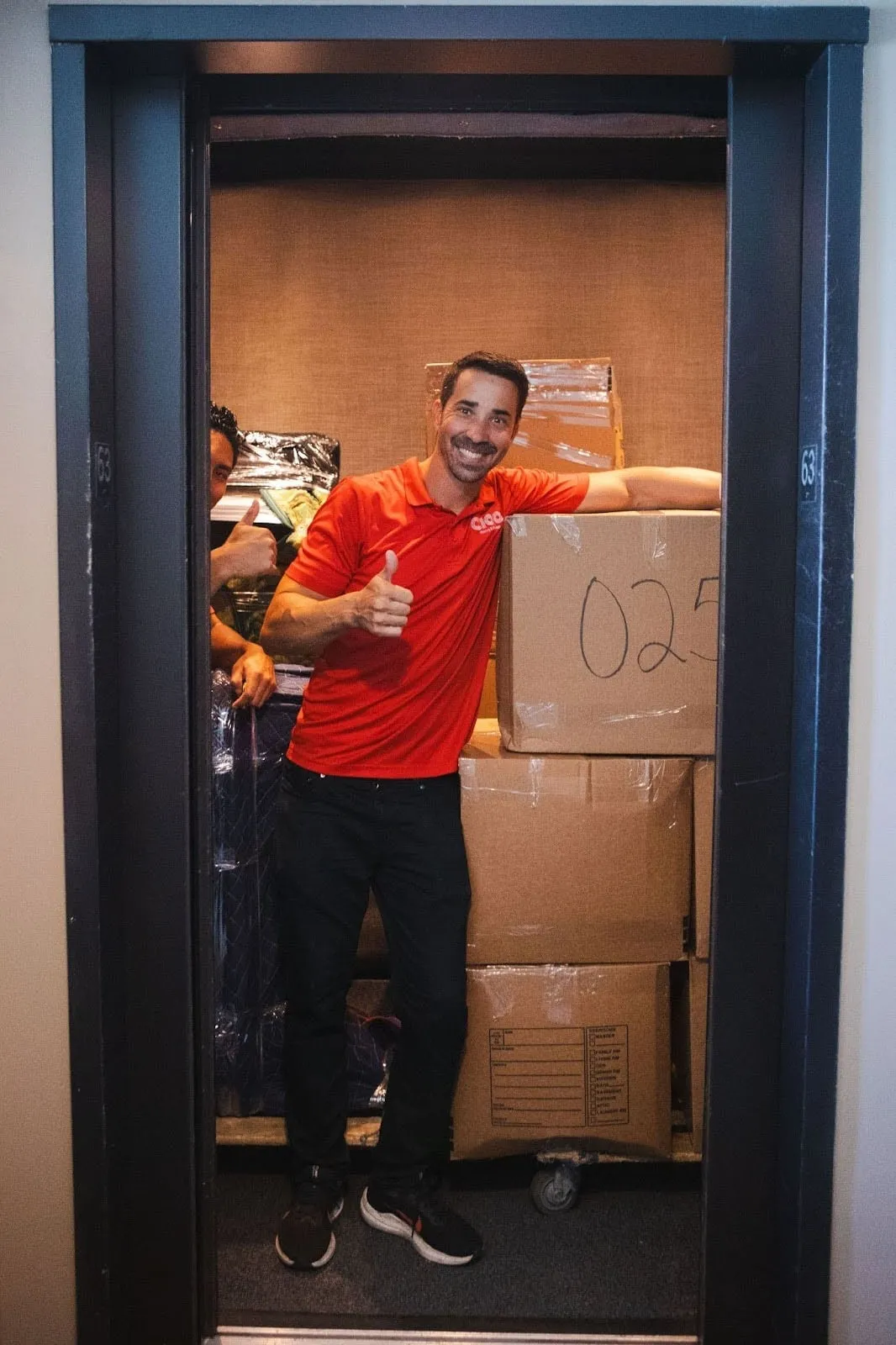 Smiling Ciao mover in an elevator stacked with boxes